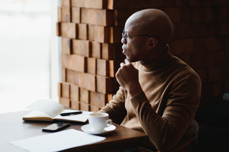 Knowledge, learning, education and technology. Casually dressed hardowrking A-student with Afro hairstyle solving mathematical problems, sitting at cafe table with textbooks and electronic deviceの写真素材