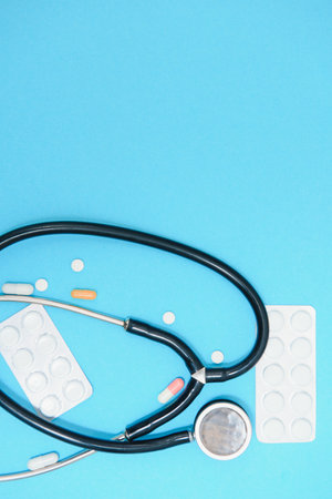 Scattered white pills on blue table.Medical, pharmacy and healthcare concept. Blue background white pills with a medical statoscope, top view.の写真素材