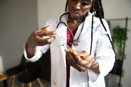 healthcare and medical concept - African doctor holding syringe with injectionの写真素材