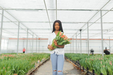 Beautiful young smiling african american girl, worker with flowers in greenhouse. Concept work in the greenhouse, flowers.の写真素材