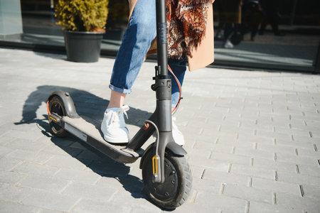 Close up of woman riding black electric kick scooter at cityscape, motion blurの写真素材