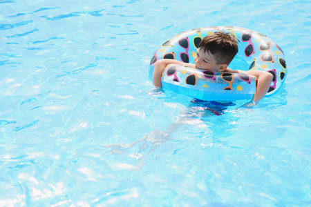 Happy boy swimming pool. Boy is alone, swimming inflatable ring and surronded by water splashes. Wet...