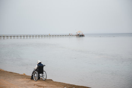 Elderly man in wheelchair on sea coastの写真素材