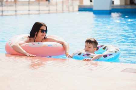Mother and baby in outdoor swimming pool of tropical resort. Kid learning to swim. Mom and child playing in water. Family summer vacation in exotic destination. Active and healthy sport for kids.の写真素材