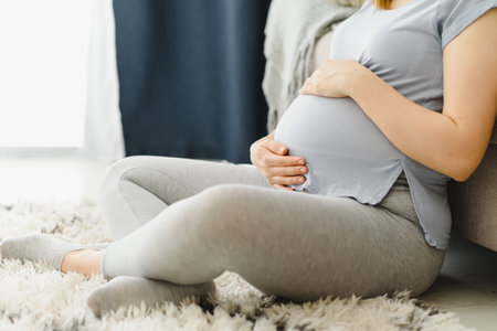 Pregnant woman caressing her belly at home. Young expectant blonde feeling her baby push, sitting on floor, copy space. Pregnancy, rest, life, expectation conceptの写真素材