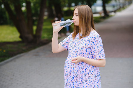 Pregnant woman stands in the park with a bottle of water. copy spaceの写真素材