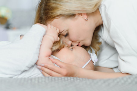Young tender happy mother hugging her newborn baby smiling sitting on bed in the morning.の写真素材