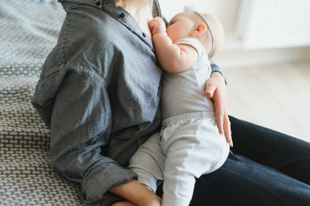 Breastfeeding Concept. Beautiful young woman lactating her toddler baby on couch at home, copy space