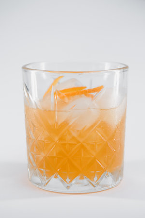 Glass of Boulevardier cocktail with big ice cube and orange zest, classic cocktail Boozy Boulevardier with Orange and Vermouth isolated on white background.の写真素材