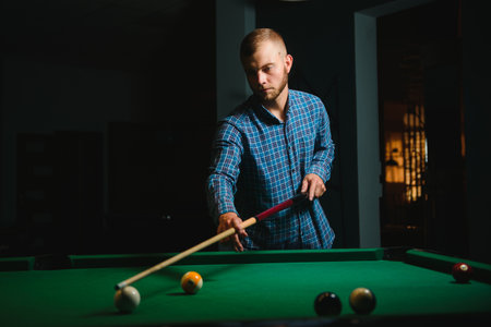 Young man playing billiards in the dark billiard club