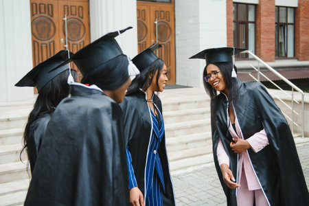 young graduates standing in front of university building on graduation dayの写真素材