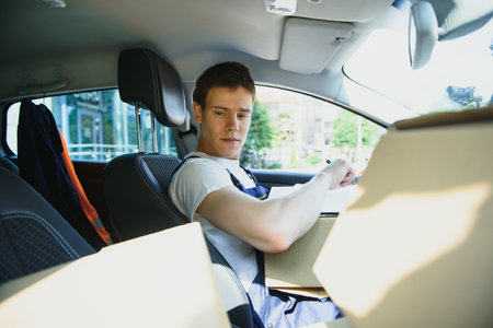 Young courier with clipboard and parcels in delivery car