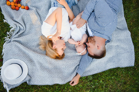 a young family lies on a blanket in a summer park