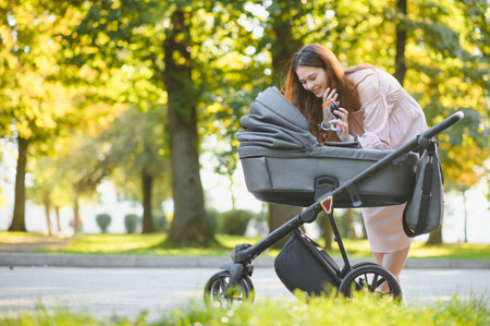 beautiful and young woman mother and baby in a stroller walking in the parkの写真素材