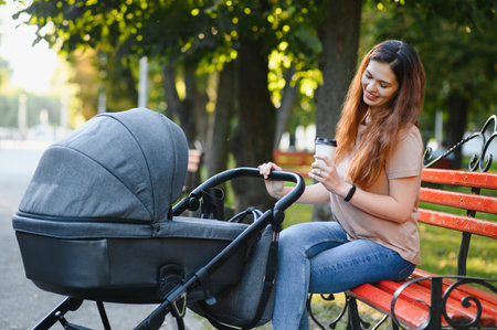 Mum sitting on a bench. Woman pushing her toddler sitting in a pram. family concept.の写真素材