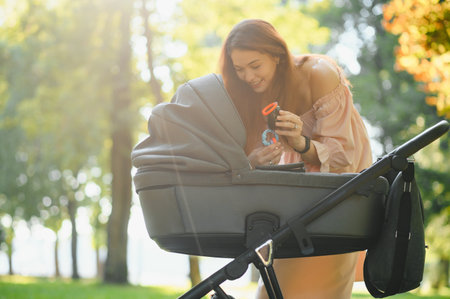beautiful and young woman mother and baby in a stroller walking in the parkの写真素材