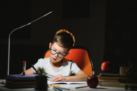 Boy learn lessons in the home setting at the table in the light of a table lamp.