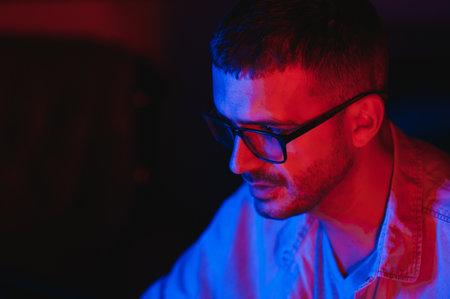 Professional Gamer Plays Video Game on His Computer. He's Participating in Online Cyber Games Tournament or in Internet Cafe. He Wears Glasses and Talks into Microphone.の写真素材