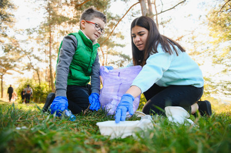 Mom teaches her son to clean up trash in nature. A woman removes plastic bottles in a bag. The topic of environmental pollution by garbage.の写真素材