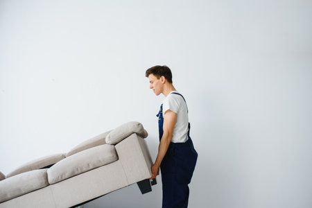 Loader moves sofa, couch. worker in overalls lifts up sofa, white background. delivery service concept. Courier delivers furniture in case of move out, relocation.の写真素材
