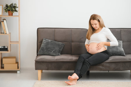 Beautiful pregnant woman sitting on sofa and holding hand on belly.の写真素材