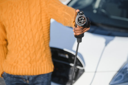 Close up of male hand holding electric charging plug for luxury red car. African businessman...