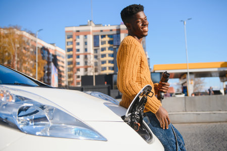 Urban, electric vehicle, eco concept. Young black skinned man, waiting for his electric car chargingの写真素材