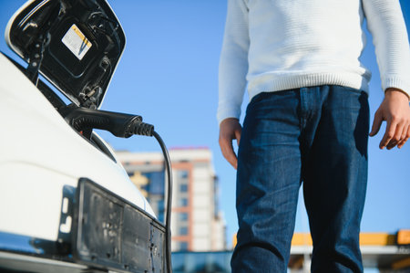 young handsome man holding charging cable at electric charging station point standing near his new car.の写真素材