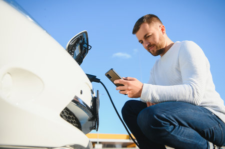 young handsome man holding charging cable at electric charging station point standing near his new...