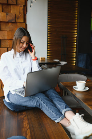 Photo portrait of gorgeous attractive woman working on laptop typing sitting in cafe drinking coffeeの写真素材