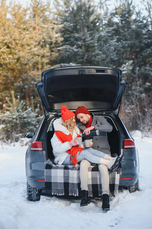 Cute Couple Having Winter Forest Picnic Drinking Tea from Tea Take Away Cup. nature picnic. Love Story Date at Car.の写真素材