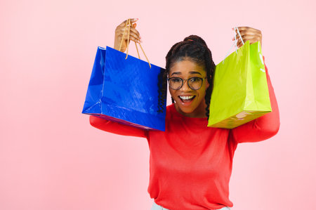 Beautiful cheerful african american woman with piles of paper bags in hands having fun enjoying...