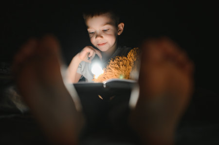Reading book and using flashlight. Young boy in casual clothes lying down near tent at evening time.の写真素材