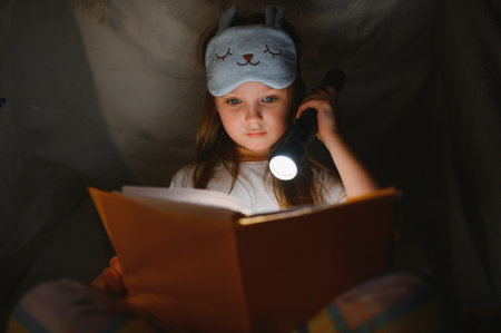 A pretty little girl reading a book on the floor under the lamp. children and education.の写真素材