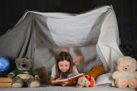 happy child girl laughing and reading book in dark in a tent at homeの写真素材