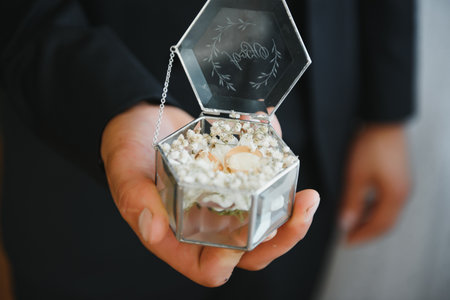 The groom on his wedding day holds two wedding rings in his hand in a hotel room. The man is wearing...
