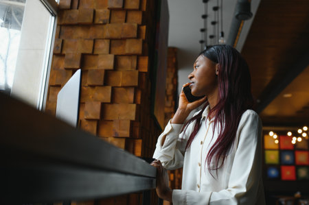Businesswoman talking to the phone in cafe. African woman with laptop in coffee shopの写真素材