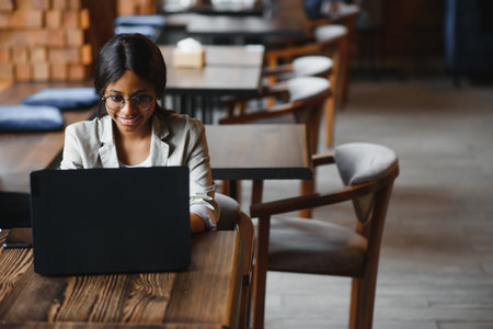 Young African American girl sitting in a restaurant and typing on her laptop. Pretty girl working on computer at cafe.の写真素材