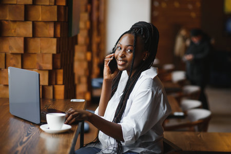 Side view of black lady enjoying morning coffee and checking emails on laptop, cafe interior, empty spaceの写真素材