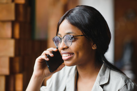 Professional African american copywriter talking about new project on mobile earning money online.Attractive dark skinned manager checking banking account talking with operatorの写真素材