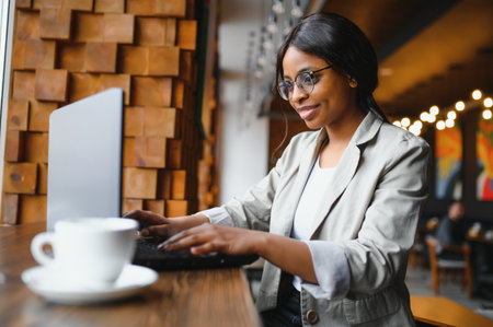 Happy african american woman worker using laptop work study at computer in loft office or cafe, smiling mixed race female student freelancer using pc app dating communicating online watching webinarの写真素材