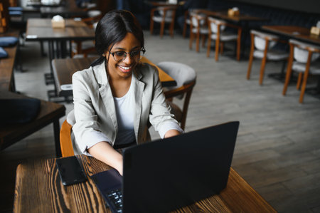 Young African American girl sitting in a restaurant and typing on her laptop. Pretty girl working on computer at cafe.の写真素材