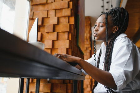 Happy african american woman worker using laptop work study at computer in loft office or cafe, smiling mixed race female student freelancer using pc app dating communicating online watching webinarの写真素材