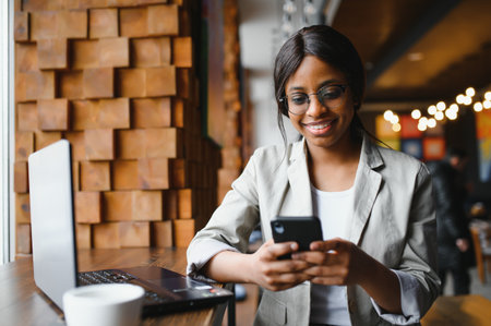 Young business woman is arranging the next business meeting in a modern coworking space by using a laptop. Young freelancer female is reading emails and other messages on a mobile phone.の写真素材
