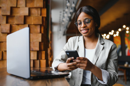 Young business woman is arranging the next business meeting in a modern coworking space by using a laptop. Young freelancer female is reading emails and other messages on a mobile phone.の写真素材