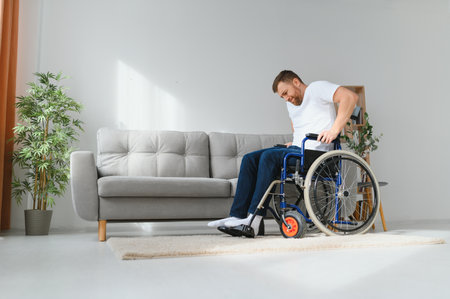 Disabled young guy trying to get up from wheelchair at home, copy space