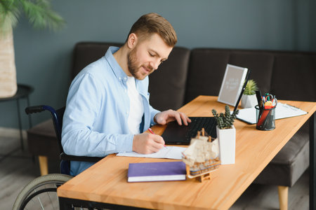 Disabled person in the wheelchair works in the office at the computer. He is smiling and passionate...