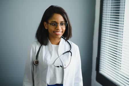 Smiling young adult indian female doctor wear white coat in medical clinic office. Happy beautiful...