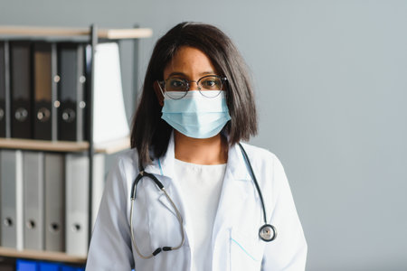 Smiling young adult indian female doctor wear white coat in medical clinic office. Happy beautiful health care india professional medic physician, therapist, headshot portrait.の写真素材