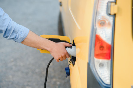 young handsome man holding charging cable at electric charging station point